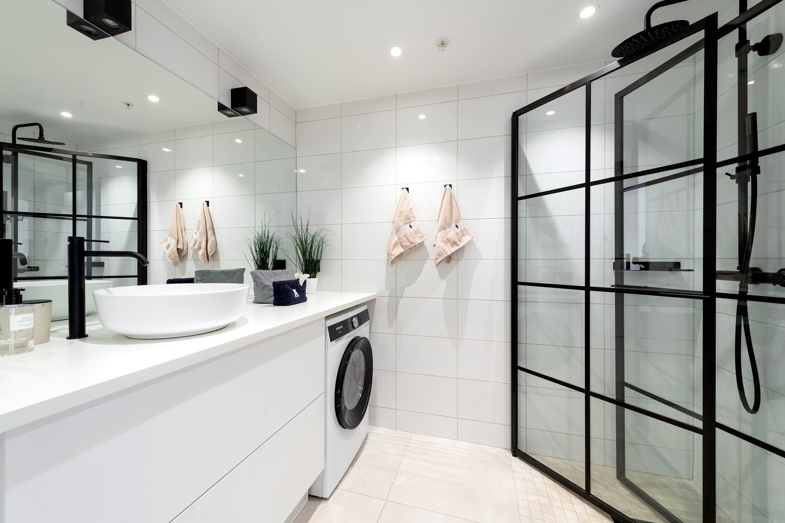 Flott flislagt bad med innadslående dusjdører og opplegg for vaskemaskin Galleribilde