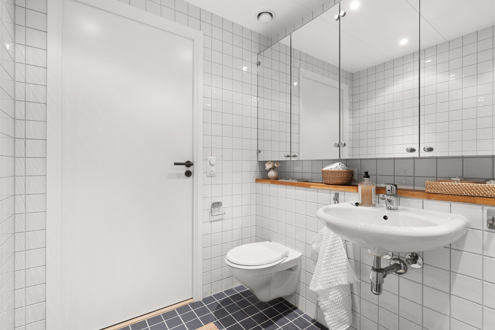 Badet har vask, vegghengt speilskap, praktisk hylle med treplate, dusjhjørne rett på flis med glassdør og vegghengt toalett. Det er god plass til vaskemaskin og tørketrommel Galleribilde