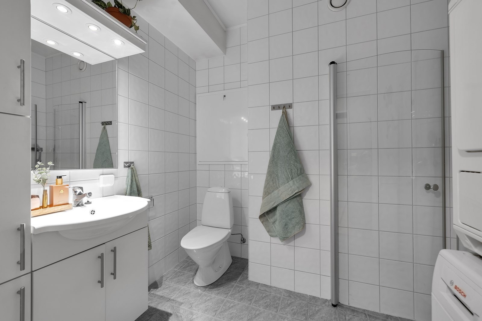 Komplett flislagt baderom med dusjnisje, opplegg vaskemaskin og praktiske innredninger. Galleribilde