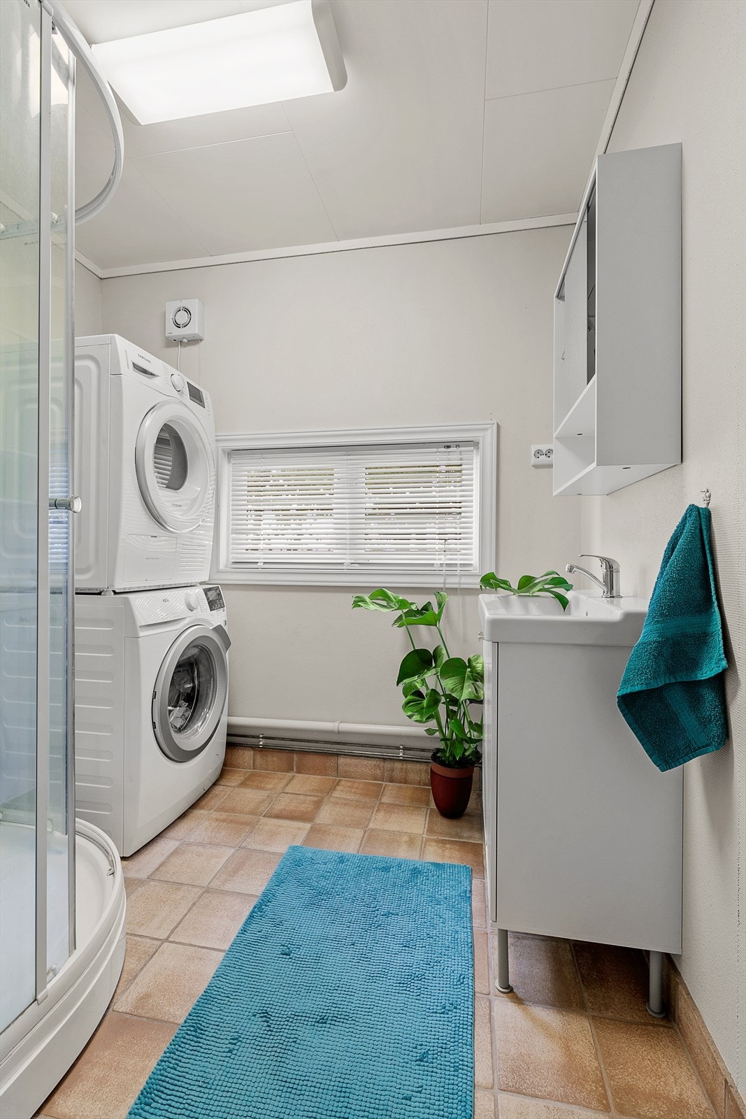 Bad/vaskerom inneholder innredning med overliggende servant, dusjkabinett og opplegg for vaskemaskin/tørketrommel Galleribilde