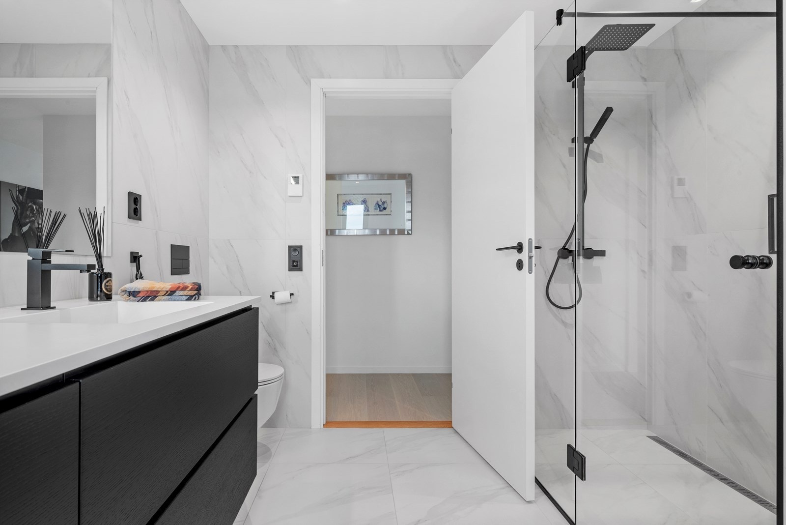 Videre byr 1.etg. på et baderom som inviterer til velvære - med marmor-inspirerte fliser, gulvvarme, elegante sorte detaljer i dusjsonen og diskret downlightbelysning. Galleribilde