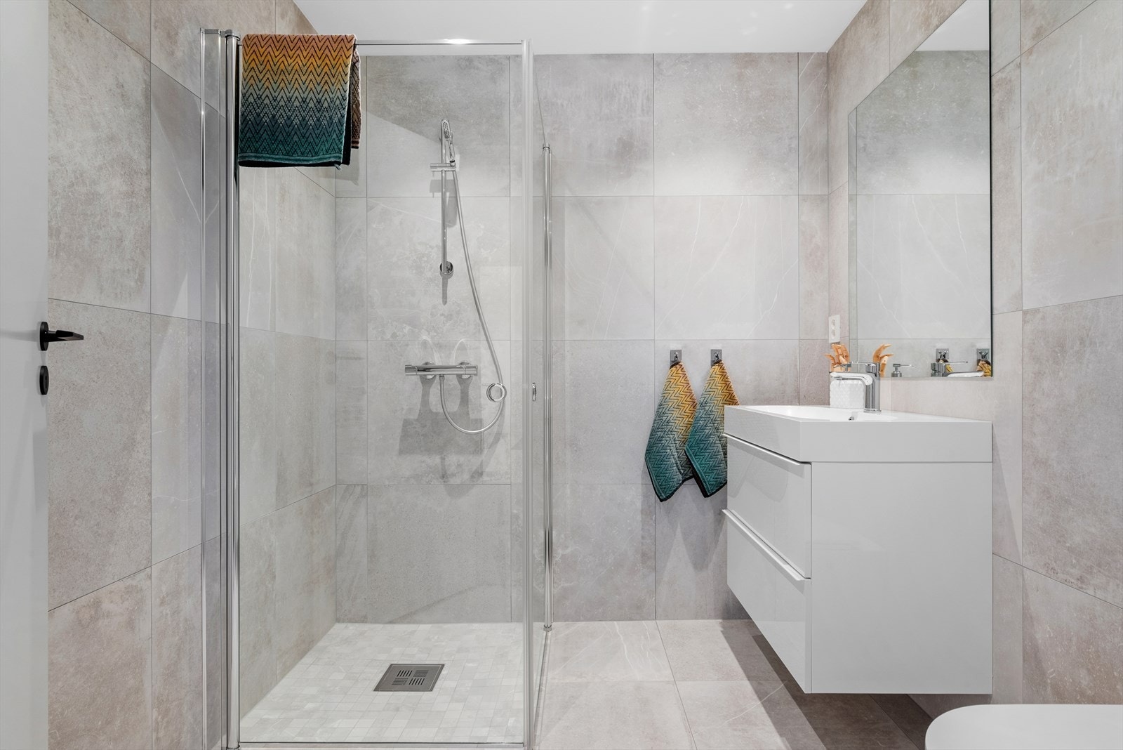 Moderne og arealeffektivt bad på 4,5 kvm, med dusjhjørne med innfellbare glassdører, servant med generøs oppbevaring og toalett. Lyse fliser og downlights gir et stilrent uttrykk. Galleribilde