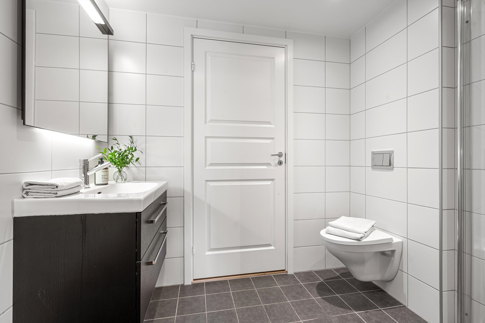 Innenfor soverommet ligger badet. Pent innredet med vegghengt toalett, servant i skuffeinnredning, speil med belysning og dusj med innfellbare dusjdører. Galleribilde
