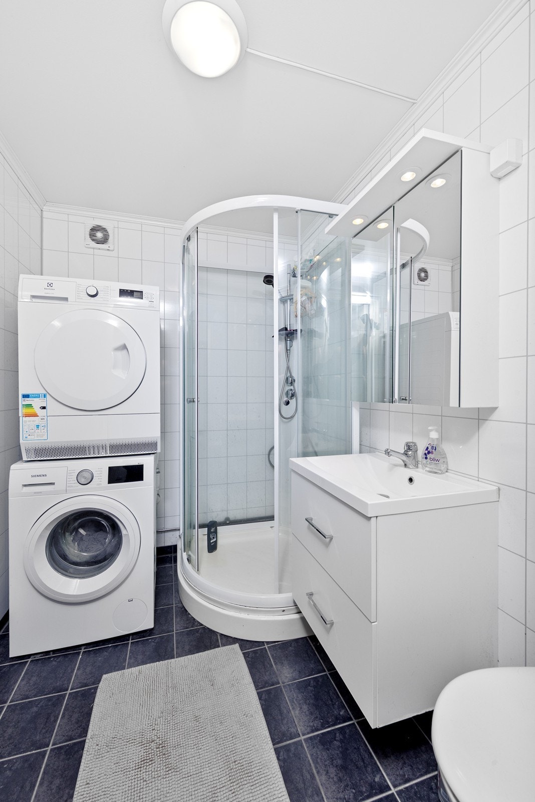 Flislagt baderom med varmekabler i gulv. Rommet har innredning med nedfelt servant, speilskap, toalett og dusjkabinett. Rommet har opplegg for vaskemaskin og tørketrommel. Galleribilde