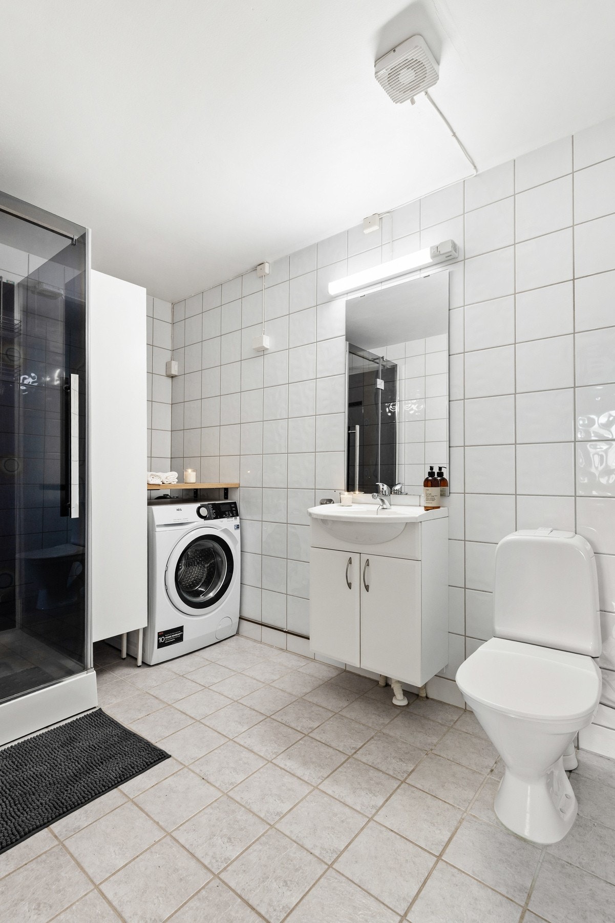 Rommet er innredet med gulvstående toalett, dusjkabinett, servantinnredning, speil og opplegg for vaskemaskin Galleribilde