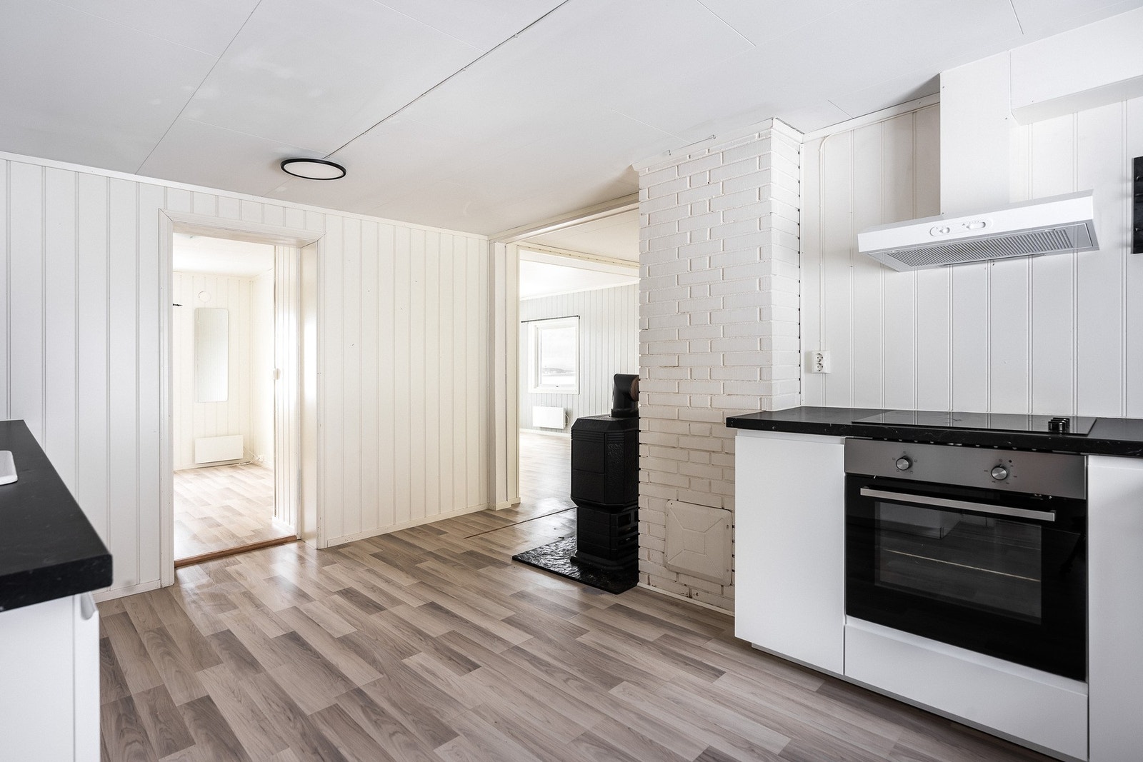 Innenfor entreen har boligen et lyst og pent kjøkken med laminatgulv og hvitmalte panelplater. Galleribilde