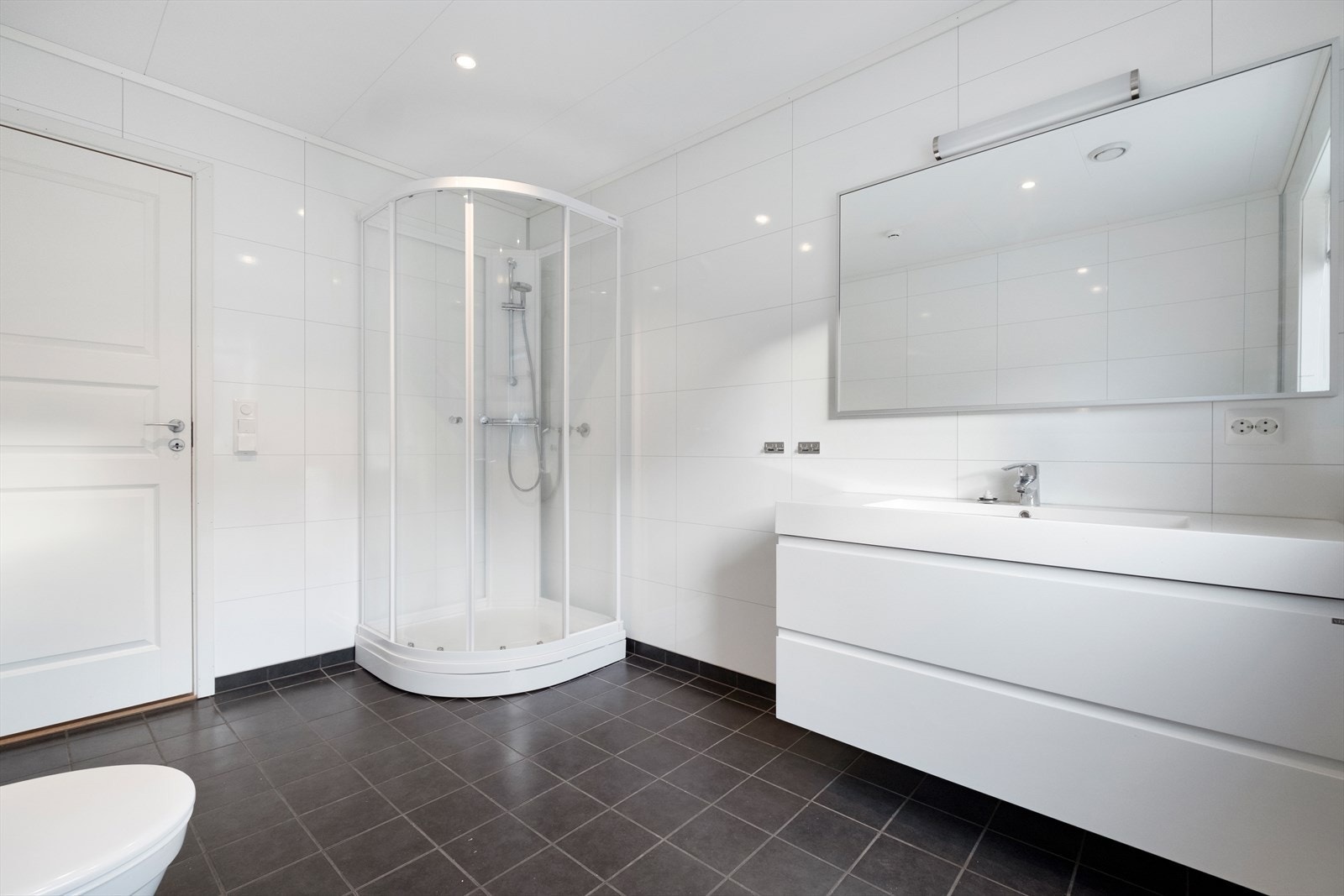 Badet er utstyrt med dusjkabinett, wc, stålskyllekum og opplegg for vaskemaskin. Galleribilde