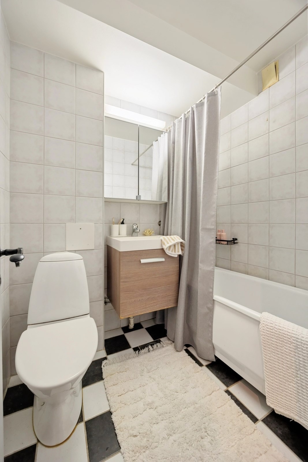 Badet er innredet med dusjløsning, servant med oppbevaring og toalett Galleribilde