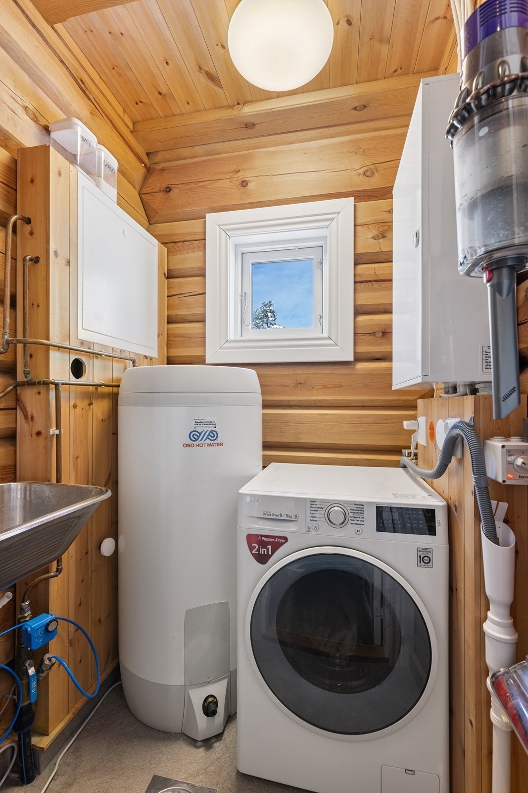 Vaskerom med fliser på gulv, innredet med servant og opplegg for vaskemaskin. Galleribilde