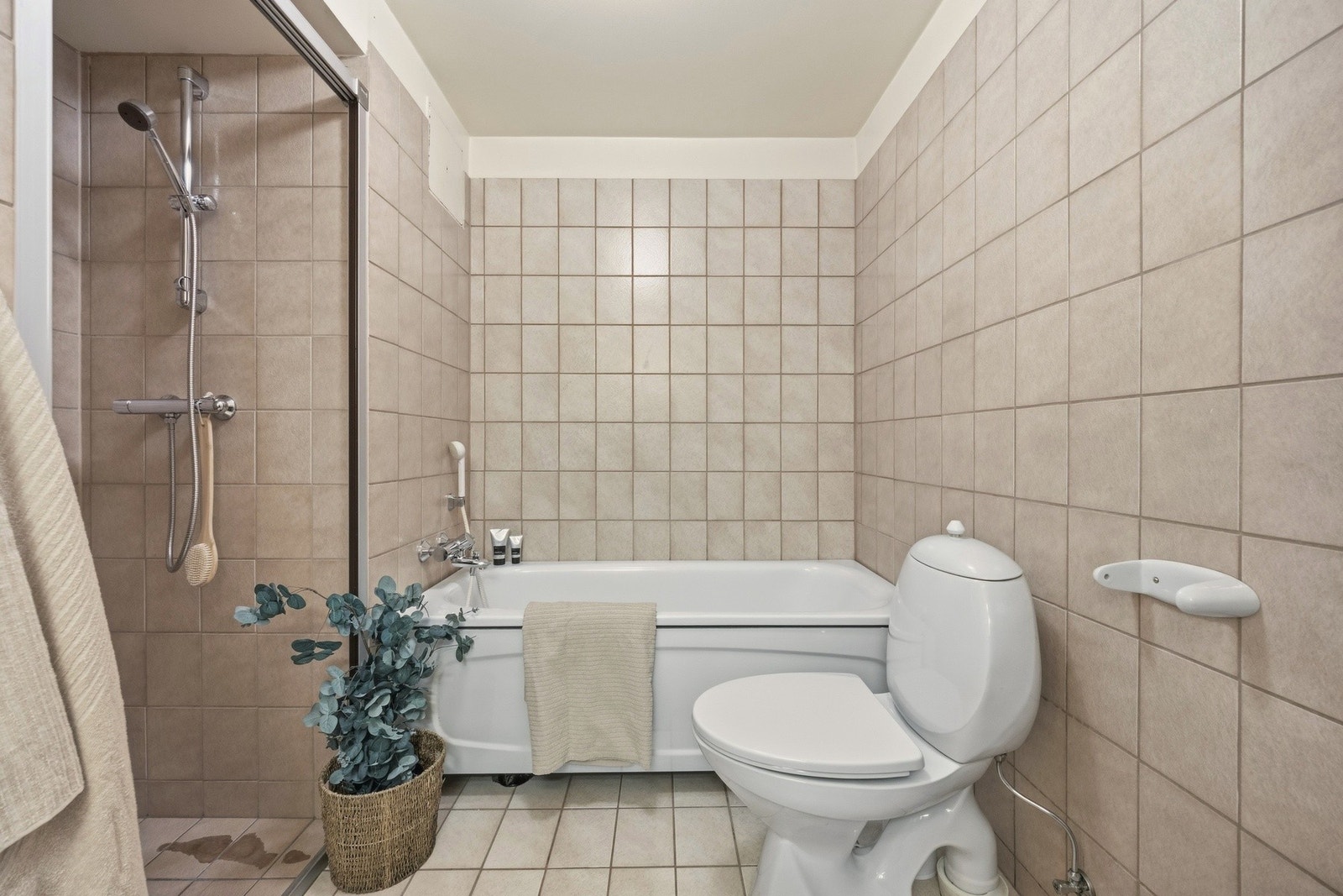 Flislagt bad med varmekabler i gulv, utstyrt med servantseksjon med skap, frittstående badekar, gulvmontert toalett og bidé. Galleribilde