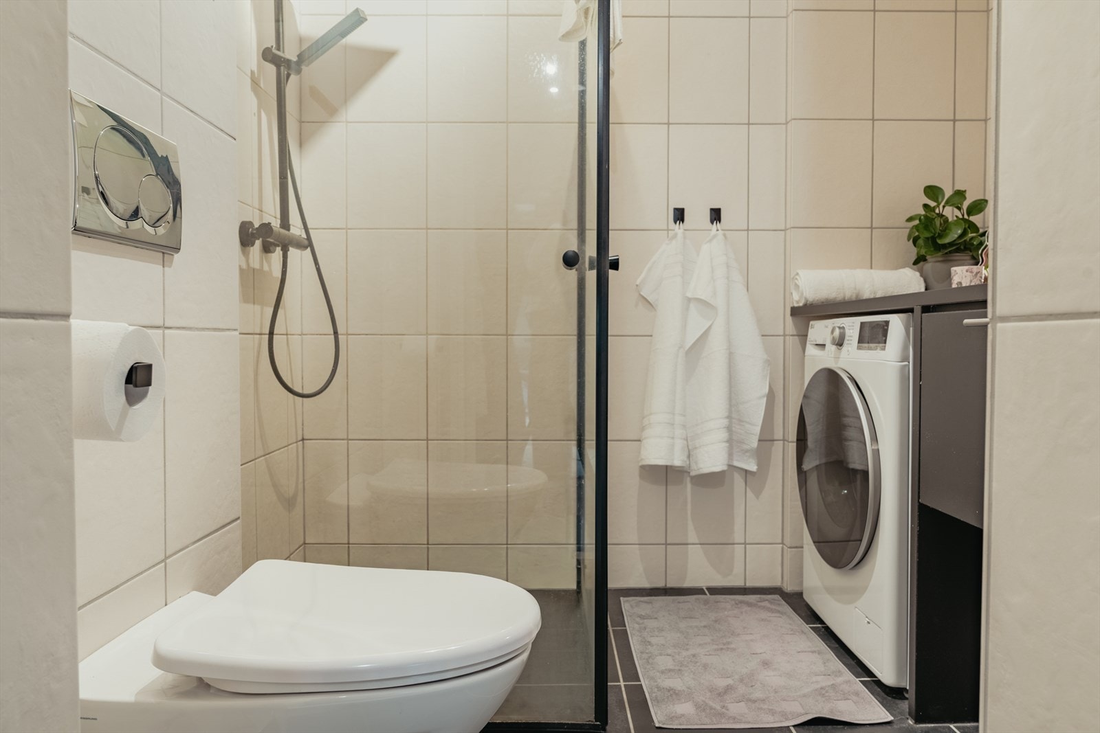 Badet er av god størrelse og er utstyrt med baderomsinnredning med servant, vegghengt toalett, dusj og opplegg for vaskemaskin Galleribilde