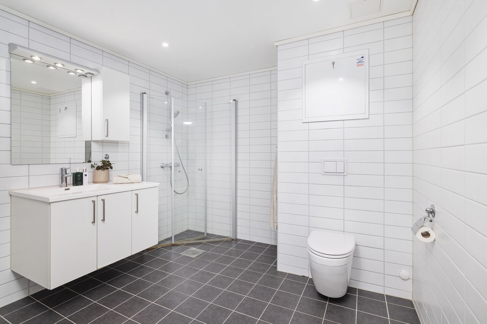 Badet er flislagt og utstyrt med gulvvarme, vegghengt toalett og dusjhjørne. Galleribilde