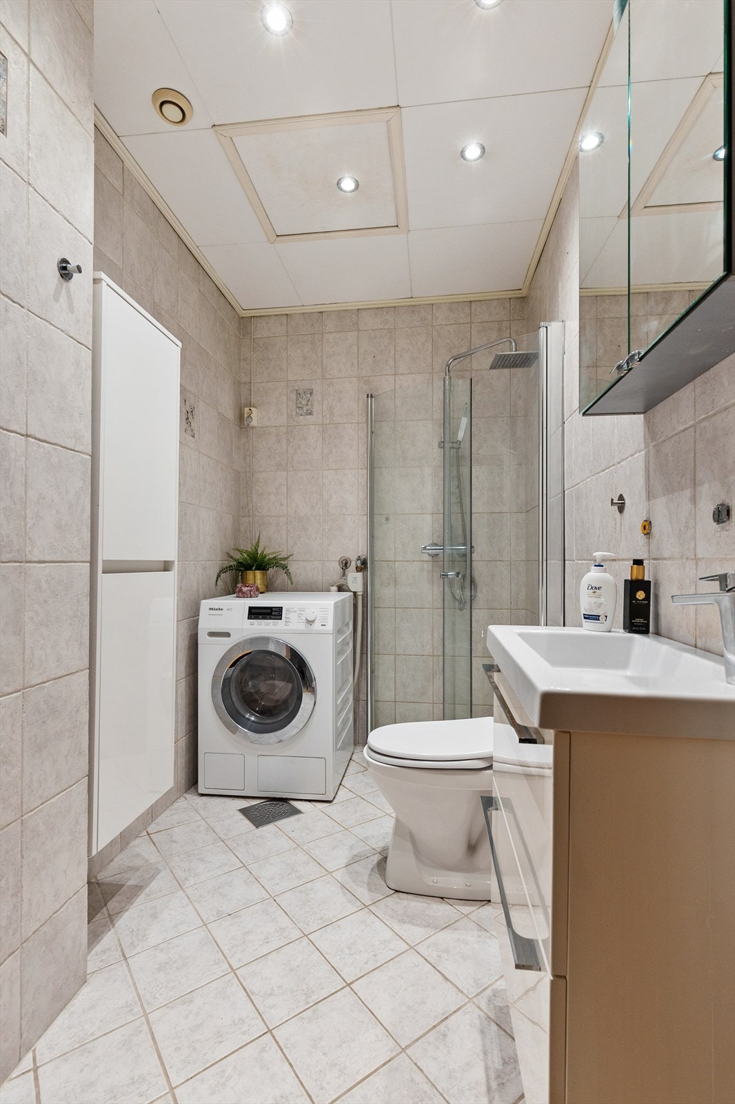 Badet er utstyrt med gulvstående toalett, dusjhjørne med svingbare glassdører og servant med innredning og speilskap. Galleribilde