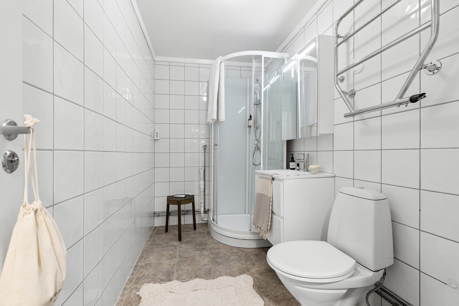 Flislagt bad innredet med servantskap, speilskap, dusjkabinett og toalett. Galleribilde