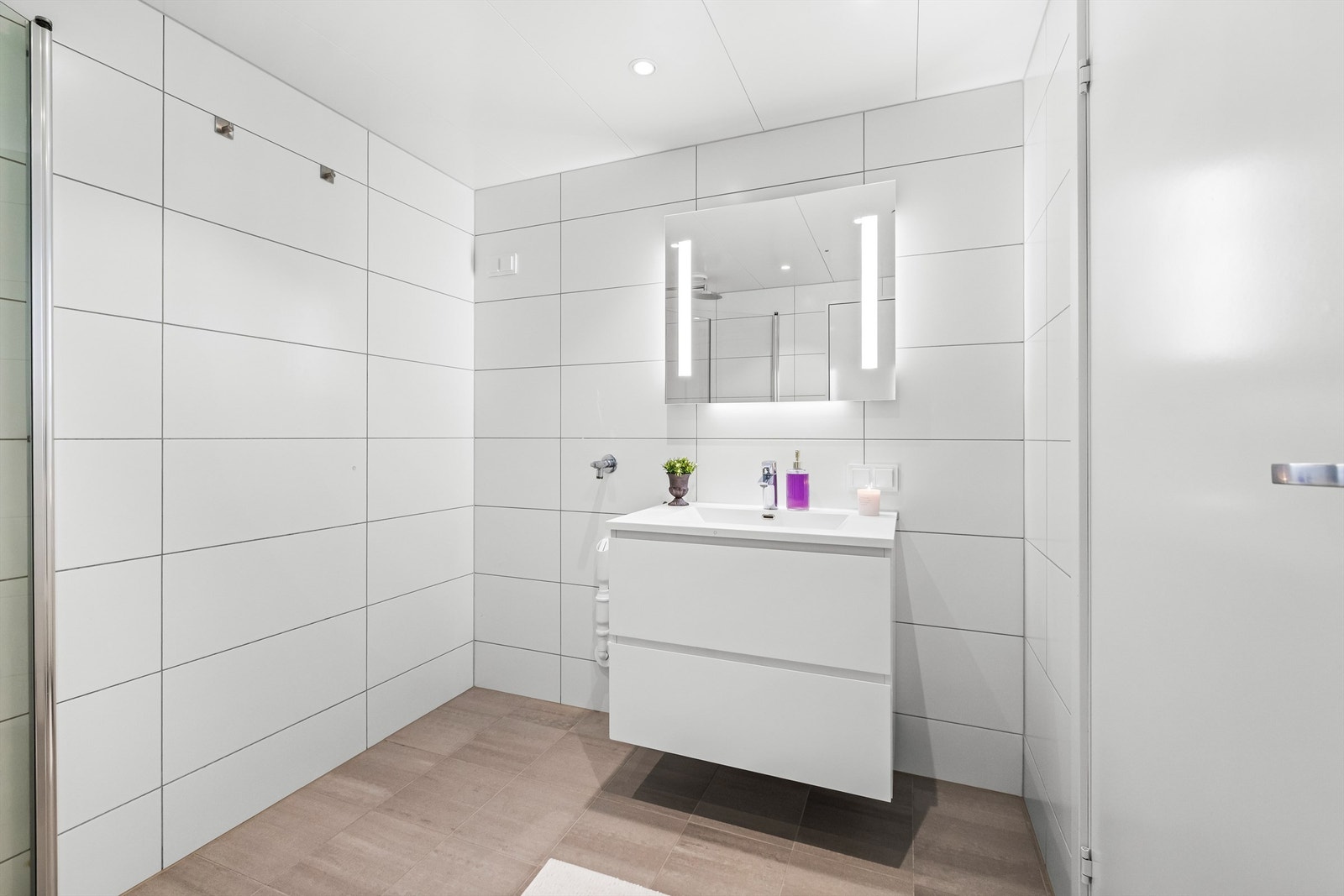 Delikat, flislagt bad fra 2023 med downlights i taket og speil med belysning. Galleribilde