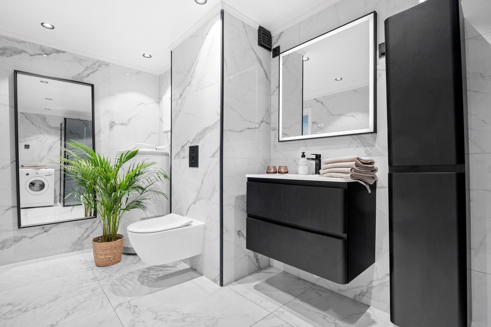 Lekkert bad med servant integrert i mørk skuffeinnredning, speil med lys og skap. Galleribilde