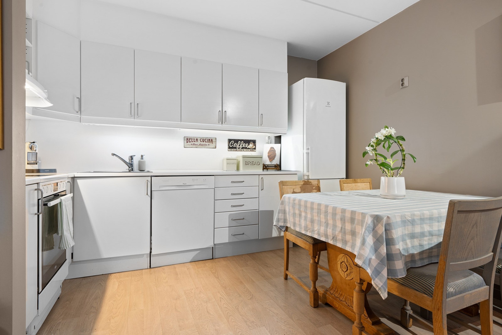 Kjøkkeninnredning med hvite slette fronter og laminert benkeplate. Benkeskapsbelysning og stikkontakter under overskap Galleribilde