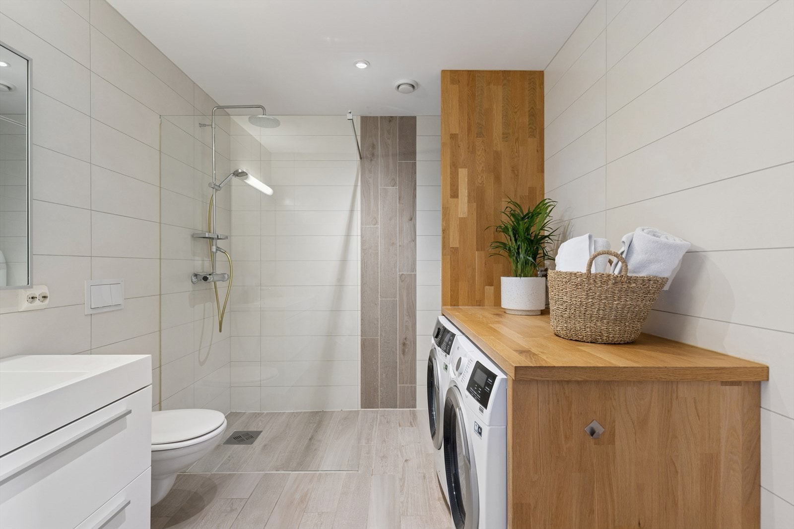 Badet er flislagt med varmekabler, spotter i taket, dusjvegg, heldekkende servant med skuffer, speil med lys og opplegg for vaskemaskin og tørketrommel. Galleribilde