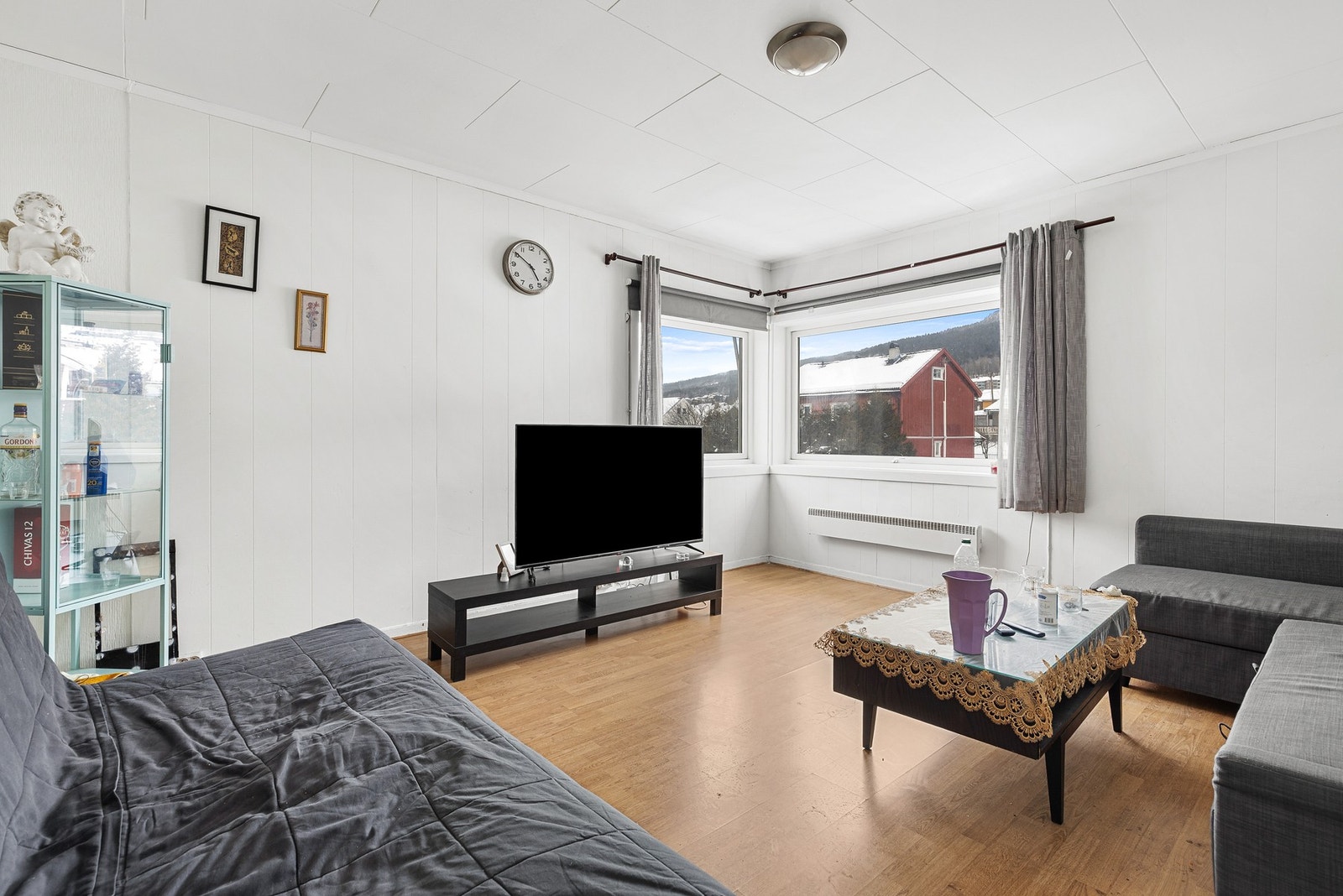 Lys stue med laminatgulv, panelplater på vegger og takplater i himling Galleribilde