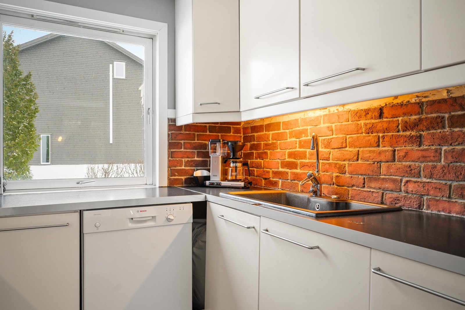 Det er montert mursteins fliser på vegg over benkeplaten på kjøkkenet.
Ventilator plassert over platetopp med avtrekk ut. Galleribilde