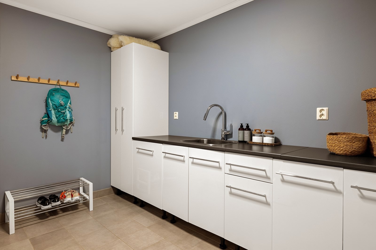 Eget vaskerom med flislagt gulv og opplegg for vaskemaskin og tørketrommel. Her er det god arbeidsplass, utslagsvask og praktisk oppbevaring, noe som gjør klesvasken mer effektiv og oversiktlig i hverdagen. Galleribilde