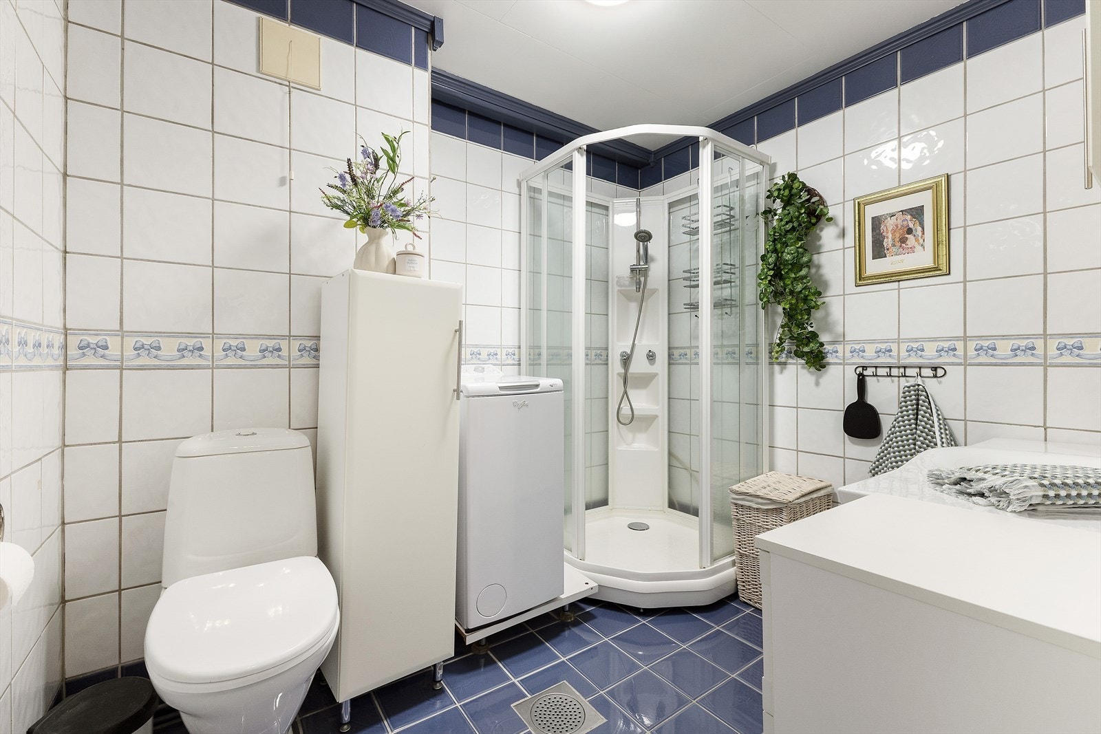 Romslig bad/vaskerom av ukjent alder. Rommet er utrustet med innredning, gulvmontert toalett, dusjkabinett og opplegg for vaskemaskin. Varmekabler i gulv. Galleribilde