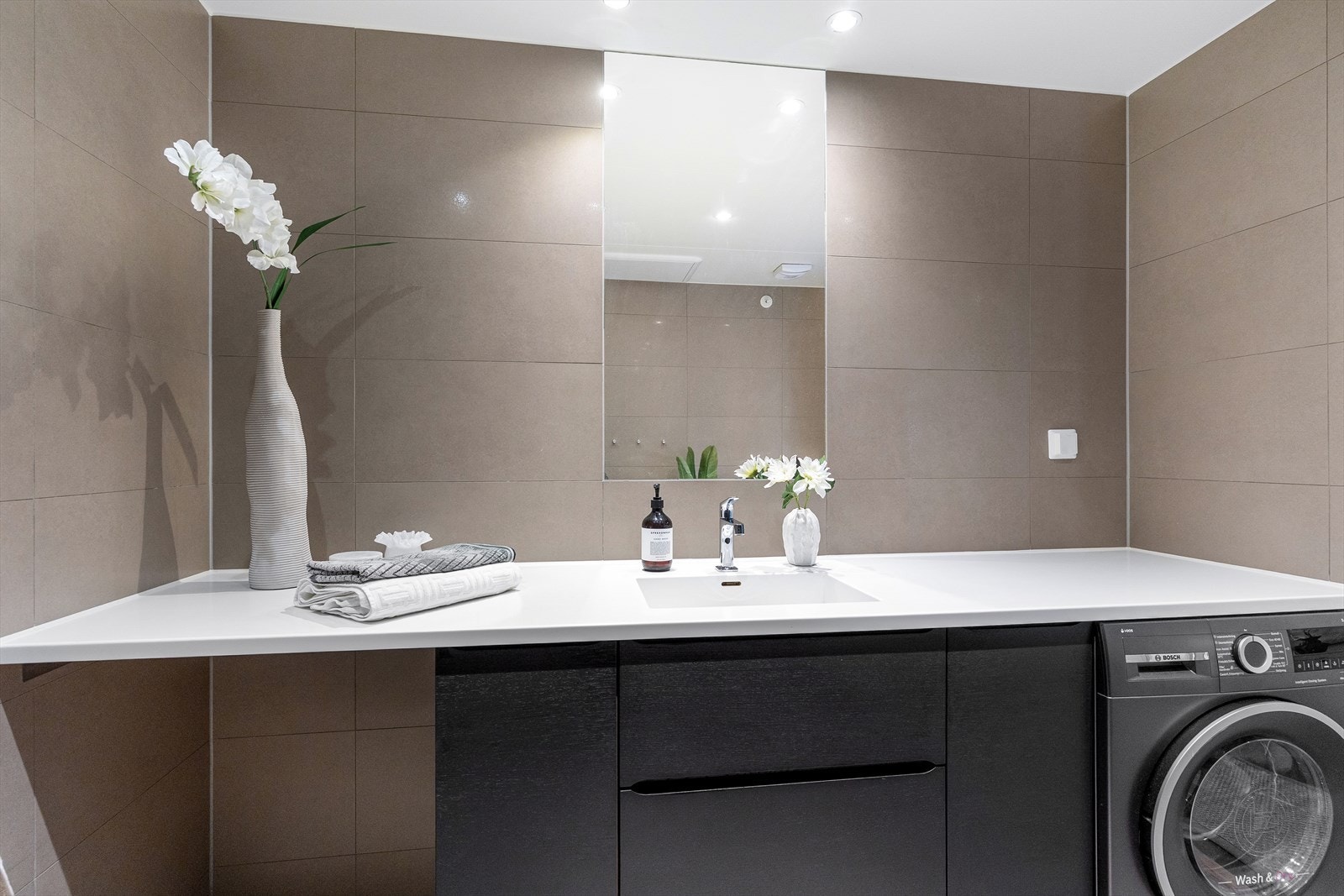 Badet er innredet med laminat benkeplate med underskap og nedfelt servant, innfelt speil, vegghengt toalett og dusjsone med innfelte dusjdører i herdet glass. Galleribilde