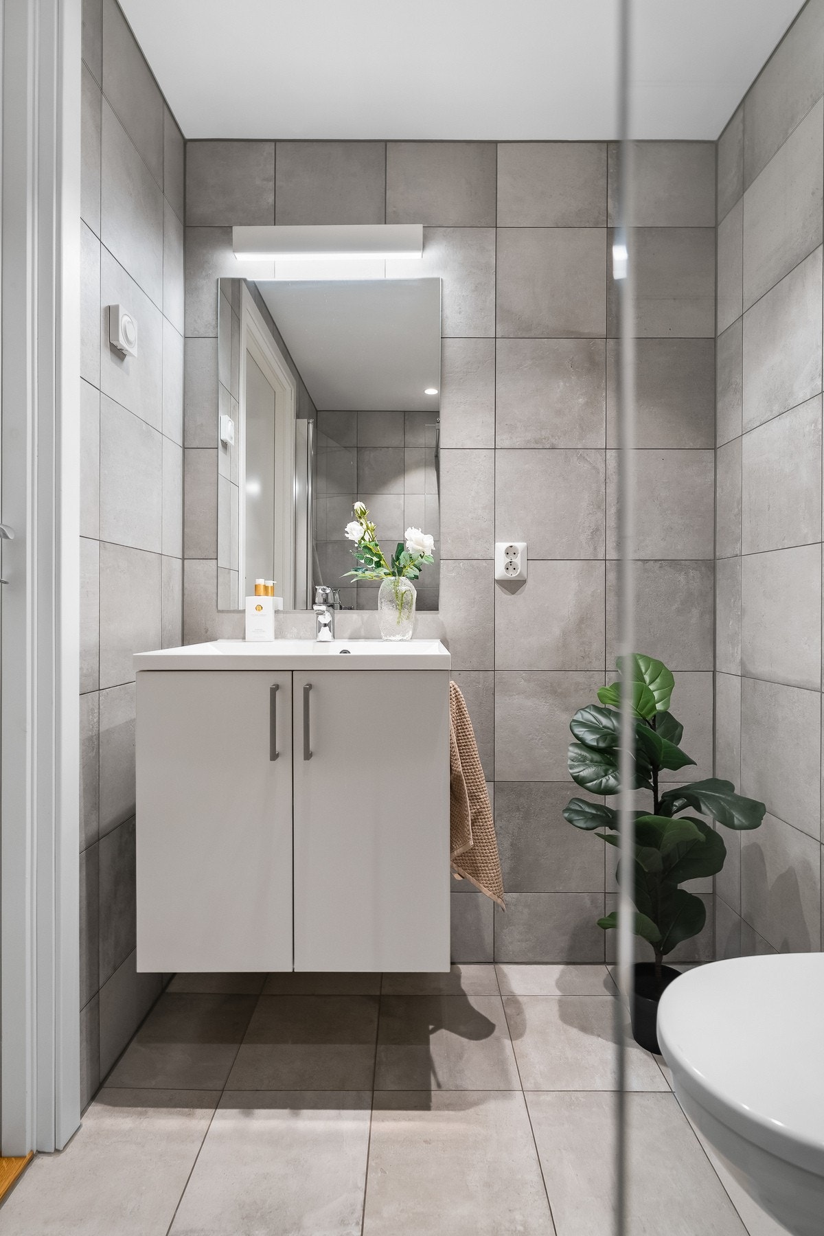 Baderommet har flislagte vegger og gulv med behagelige varmekabler. Innredningen består av servant med underskap, speil, vegghengt toalett og dusj sone. Galleribilde