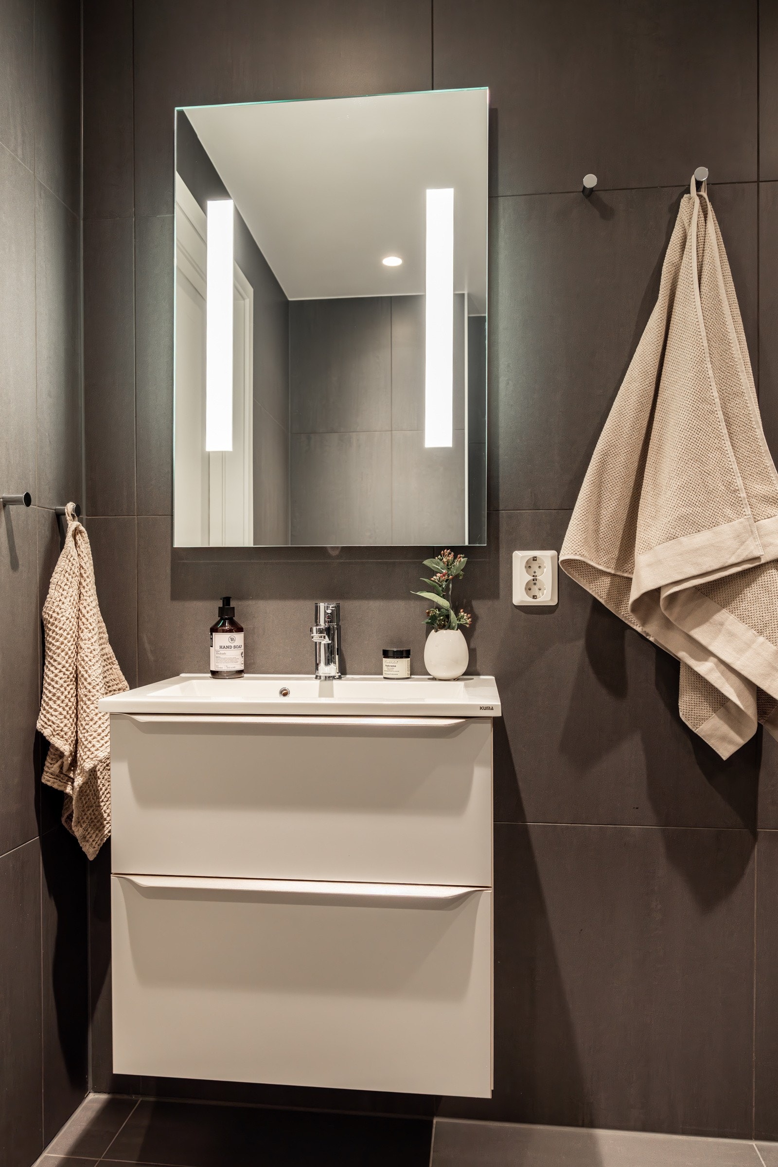 Moderne baderomsinnredning med skuffer og heldekkende servant, speil med integrert belysning over. Galleribilde