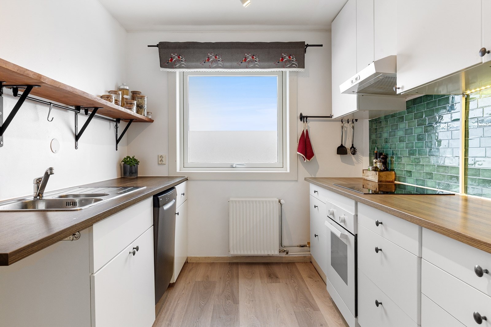 Innredning langs to vegger og stort vindu i enden. Integrert platetopp og komfyr, samt opplegg for oppvaskmaskin. Galleribilde