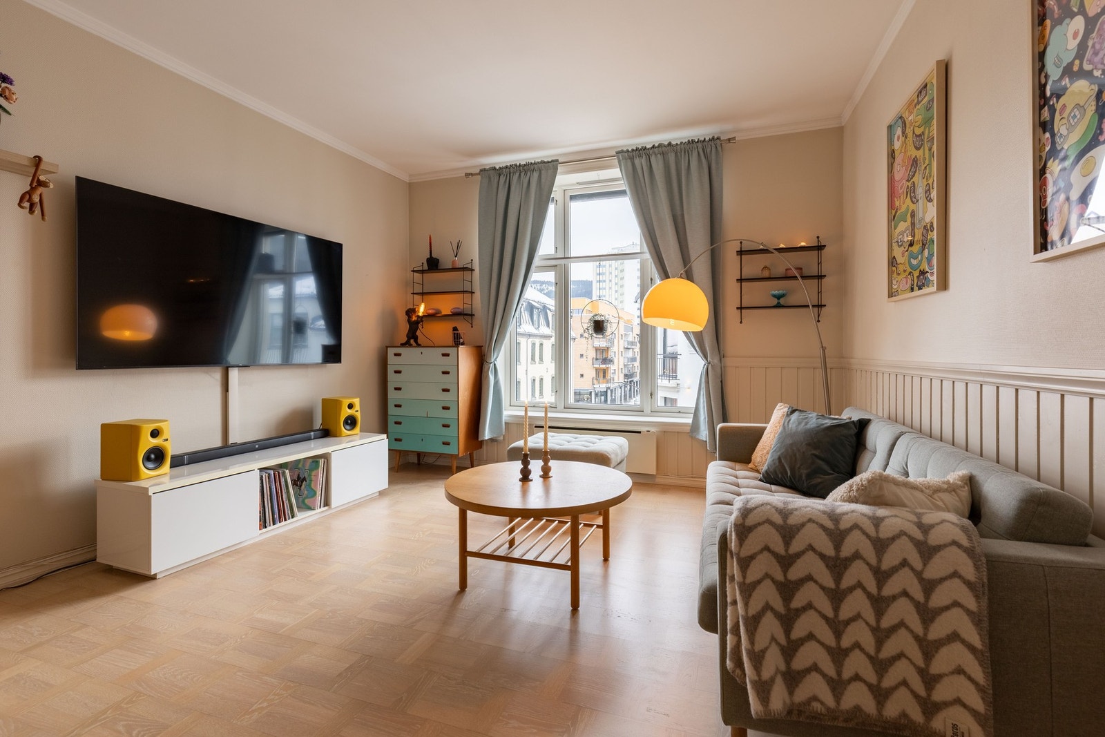 Stuen fremstår som luftig og romslig med parkett på gulv og brystpanel på deler av veggene, malt i lyse, beige nyanser. Galleribilde