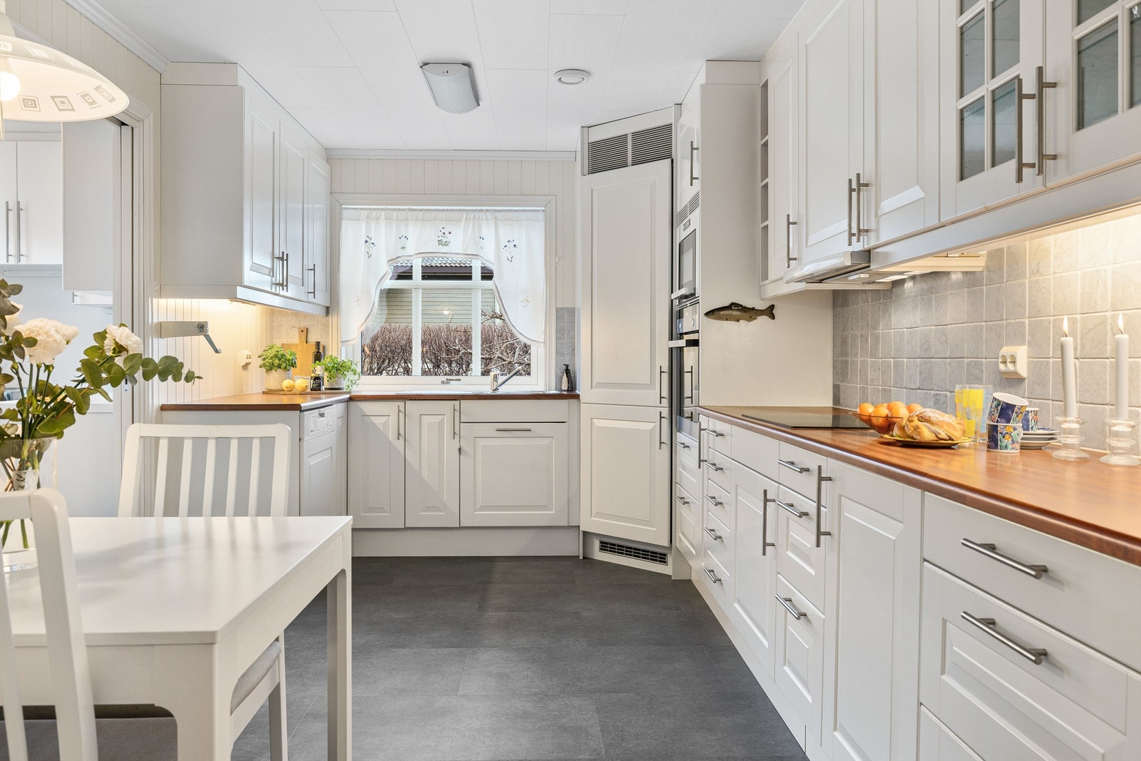 Kjøkken med stor innredning, integrerte hvitevarer og fliser mellom benk og overskap. Galleribilde