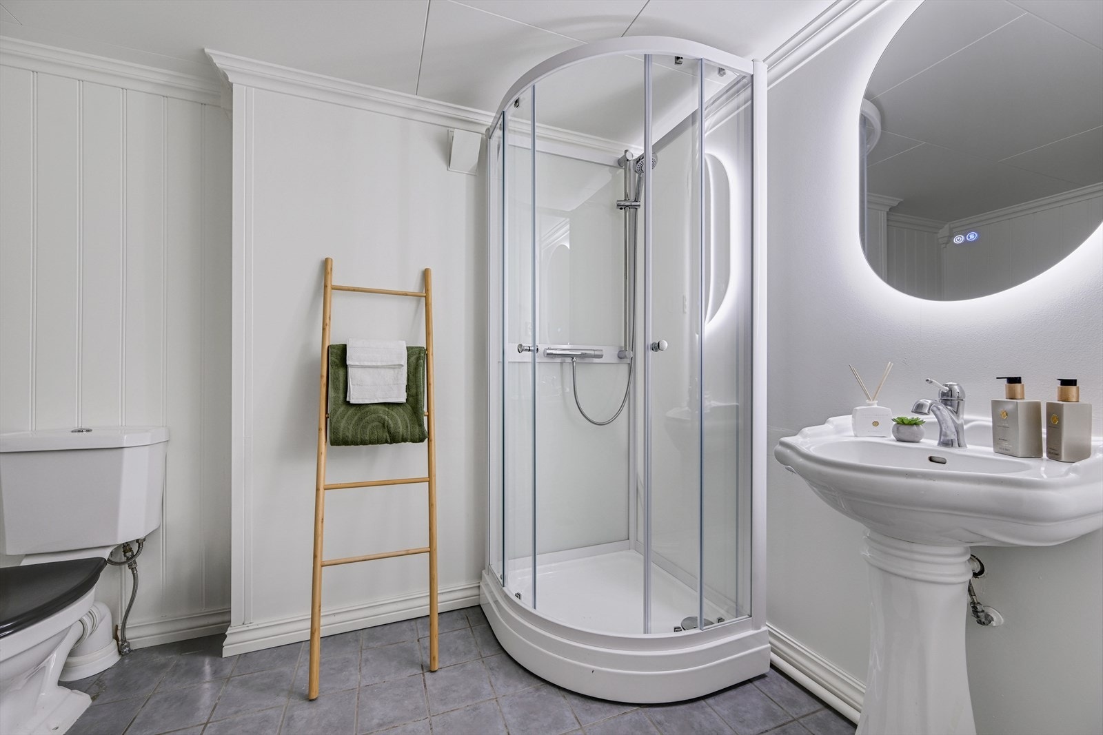 Bad med fliser på gulv, malte plater og panel på veggene og takess i taket. Toalett, servant og dusjkabinett. Galleribilde