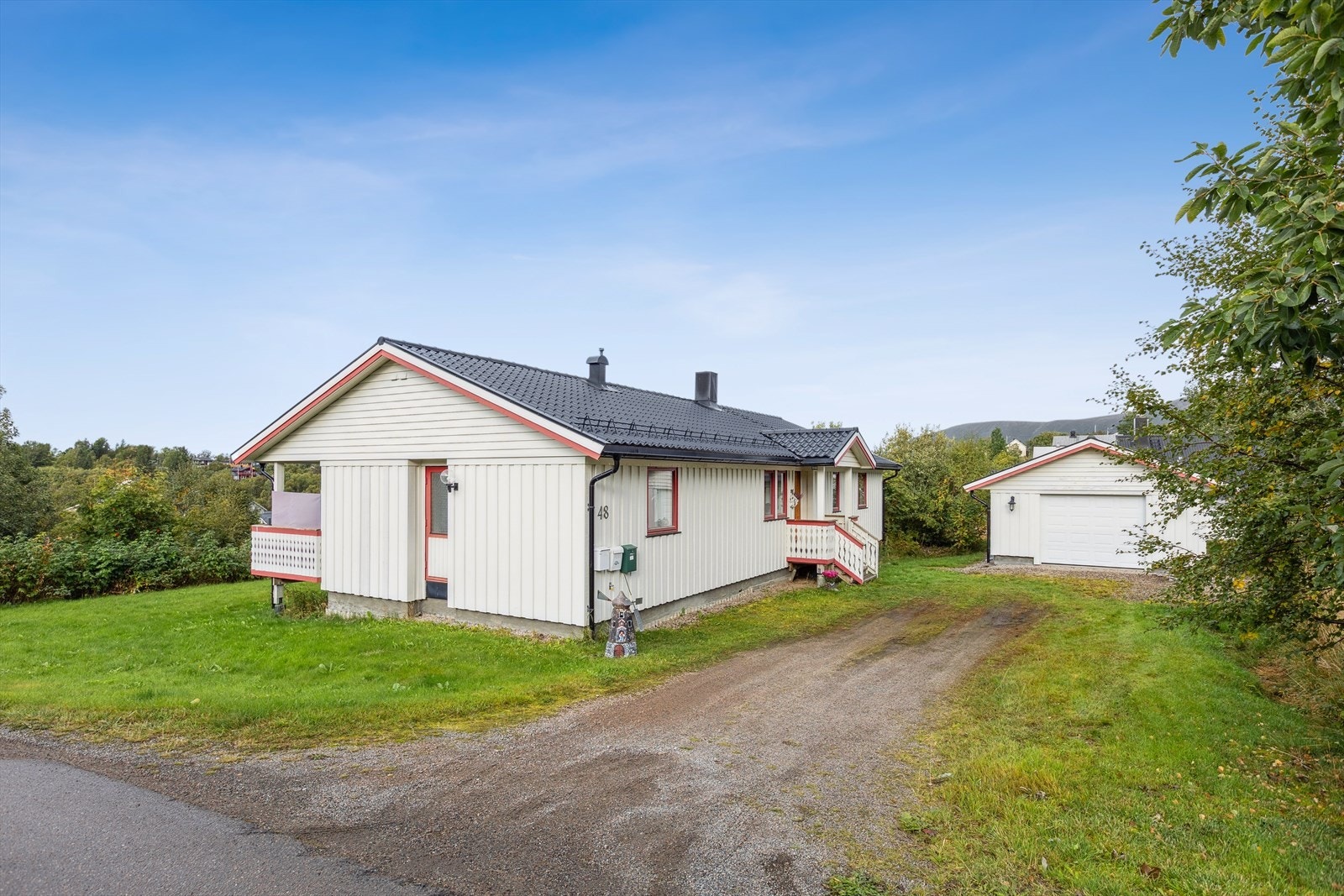 Tomten ligger på en liten høyde omgitt av skog som hindrer innsyn. Gruset nedkjørsel til garasjen. Galleribilde
