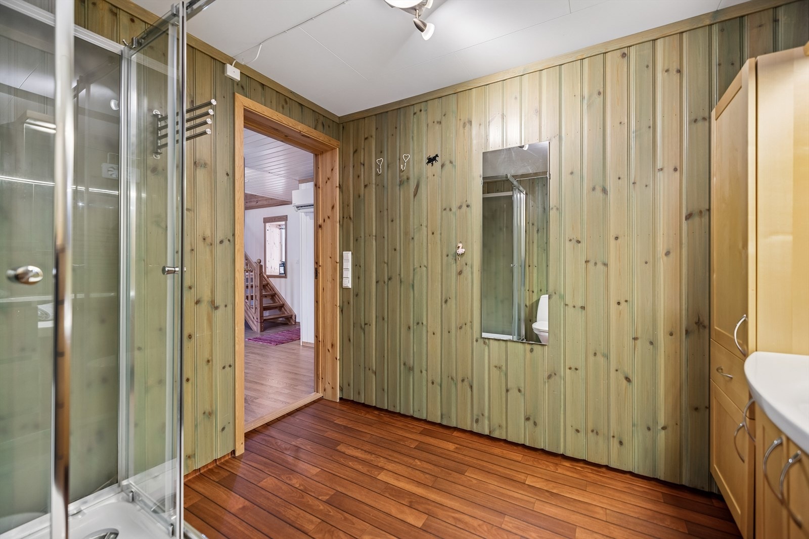Rommet er utstyrt med dusjkabinett, servantskap og vegger kledd med behandlet trepanel. Galleribilde