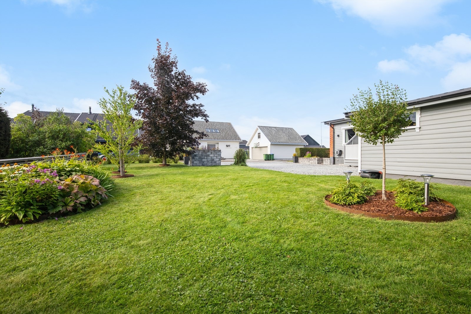 Pent opparbeidet hage med beplantning og trær som rammer inn eiendommen. Robotklipper medfølger ikke salget. Galleribilde