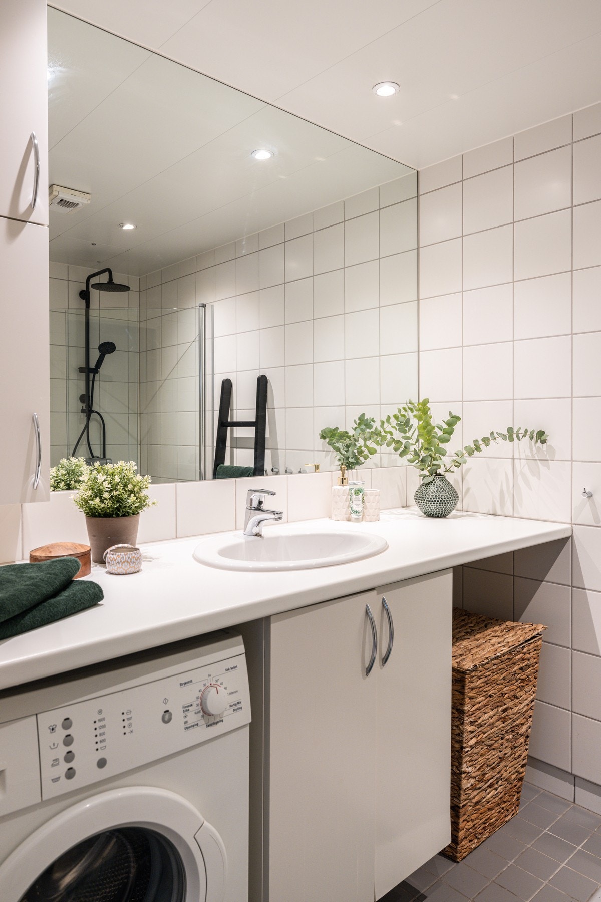 Baderomsinnredning med hvite glatte fronter og langstrakt benkplate med nedfelt servant, stort speil og vegghengt skap over. Galleribilde