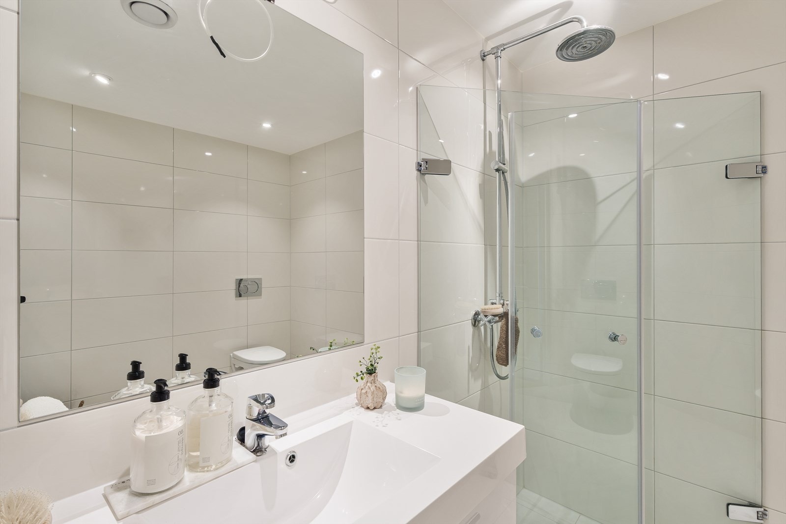 Badet er innredet med servant med tilhørende møblement og speil, vegghengt toalett og et praktisk, innfellbart dusjhjørne med dusjgarnityr. Galleribilde