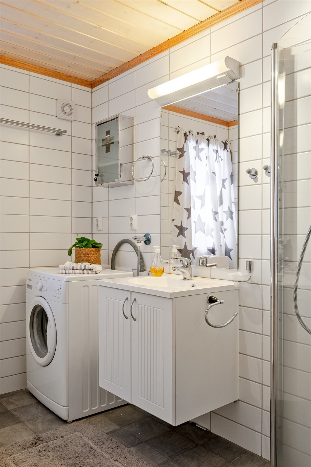 Lyst servantskap med speil og belysning over. Baderommet er også utstyrt med dusjhjørne med innfellbare glassdører og vegghengt toalett. I hjørnet er det plass og opplegg for vaskemaskin. Galleribilde