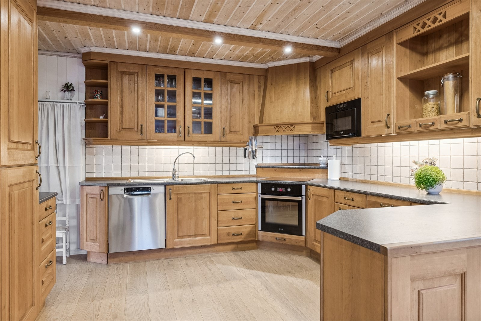 Kjøkkeninnredningen har profilerte fronter av tre, montert på folierte skrog. Benkeplaten er laminert med nedfelt dobbel oppvaskkum i stål med ett-greps blandebatteri. Galleribilde