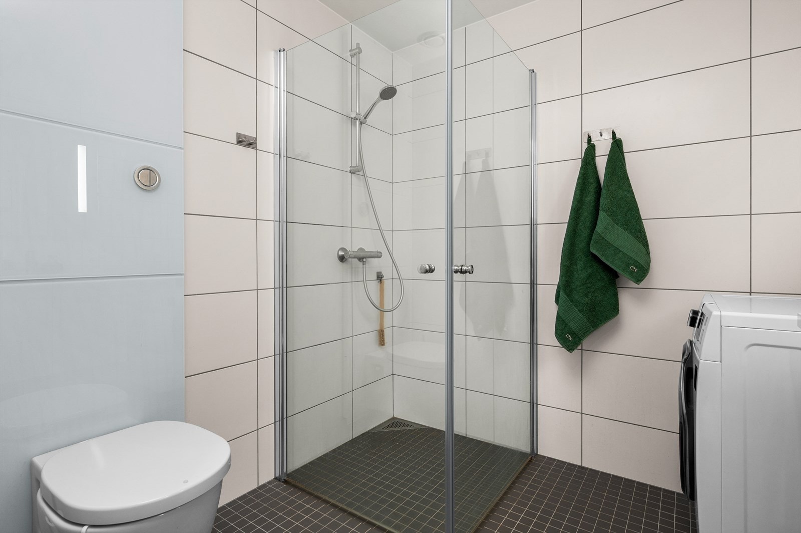 Badet er utstyrt med vegghengt toalett, dusjhjørne, speil med innfelte lys og opplegg til vaskemaskin. Galleribilde