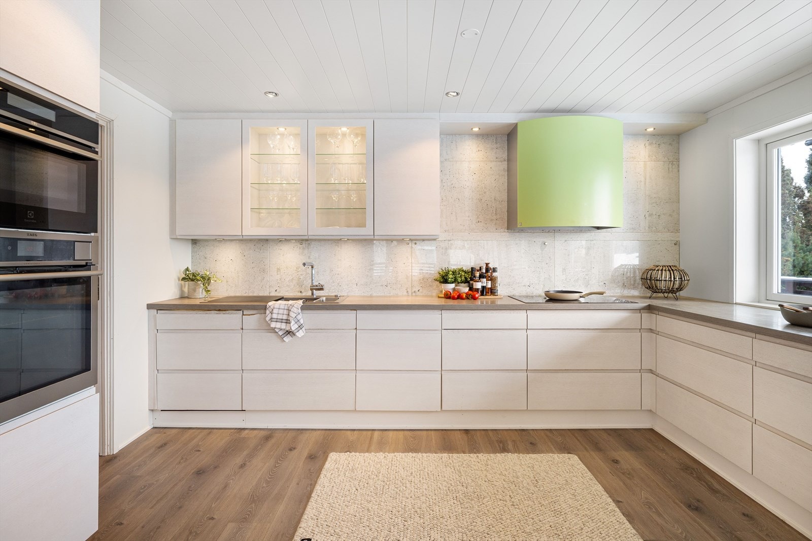 Innredningen har hvite glatte fronter og laminert benkeplate med nedfelt oppvaskkum. Praktisk med glassplater i benkeryggen og belysning under overskapene. Galleribilde