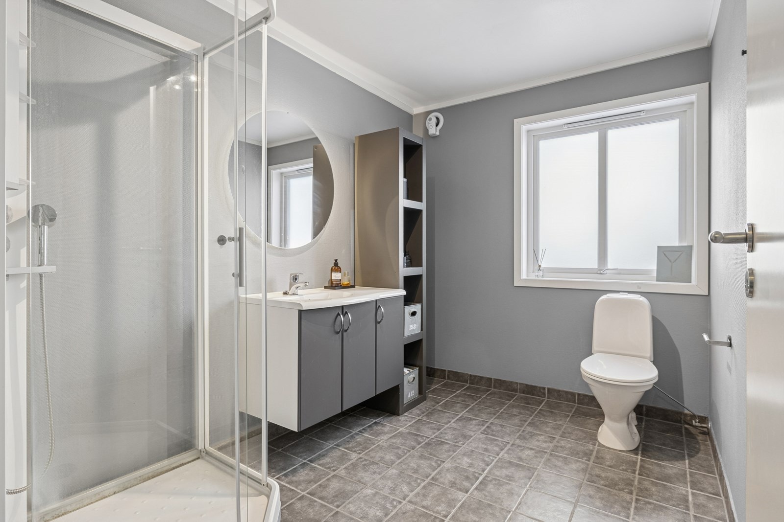 Flislagt baderomsgulv med dusjkabinett, toalett og servant. Galleribilde