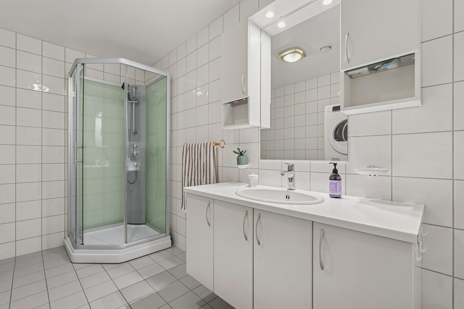 Baderommet er innredet med dusjkabinett, servant med praktisk skapinnredning, gulvmontert toalett og opplegg for både vaskemaskin og tørketrommel. Galleribilde