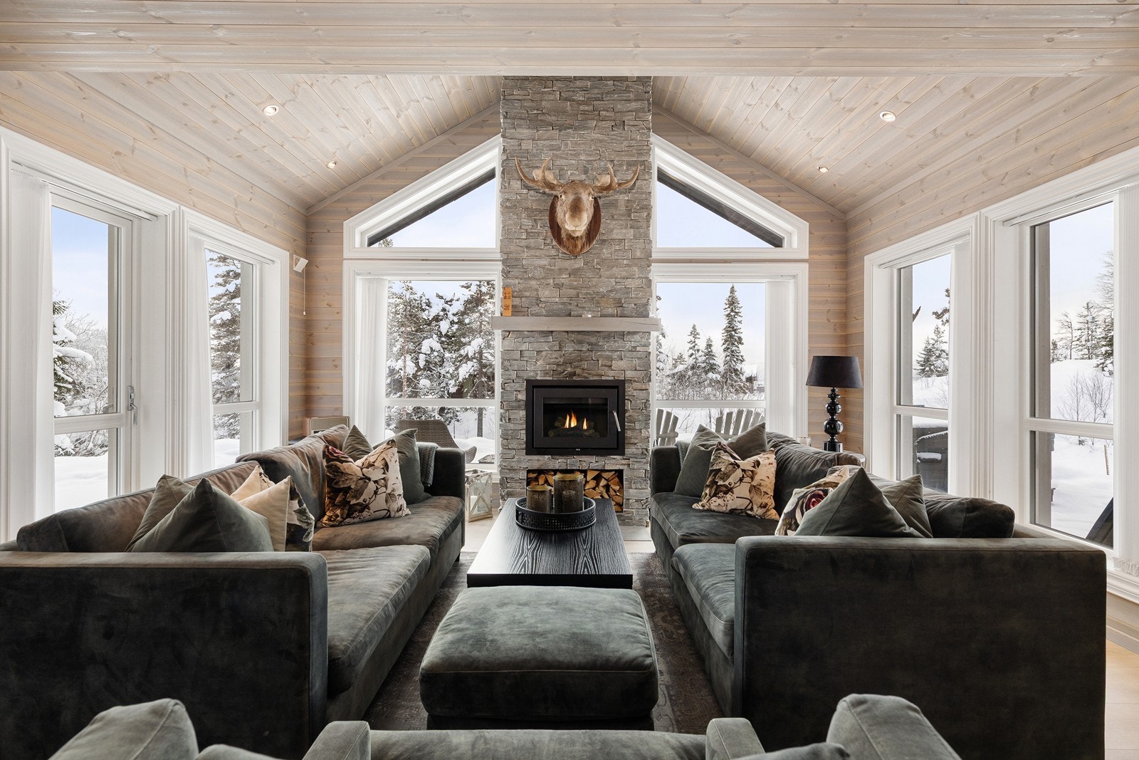 Den fantastiske peisen står som et majestetisk midtpunkt i rommet, der naturstein, høy himling og store vindusflater sammen skaper en imponerende og innbydende atmosfære. Galleribilde