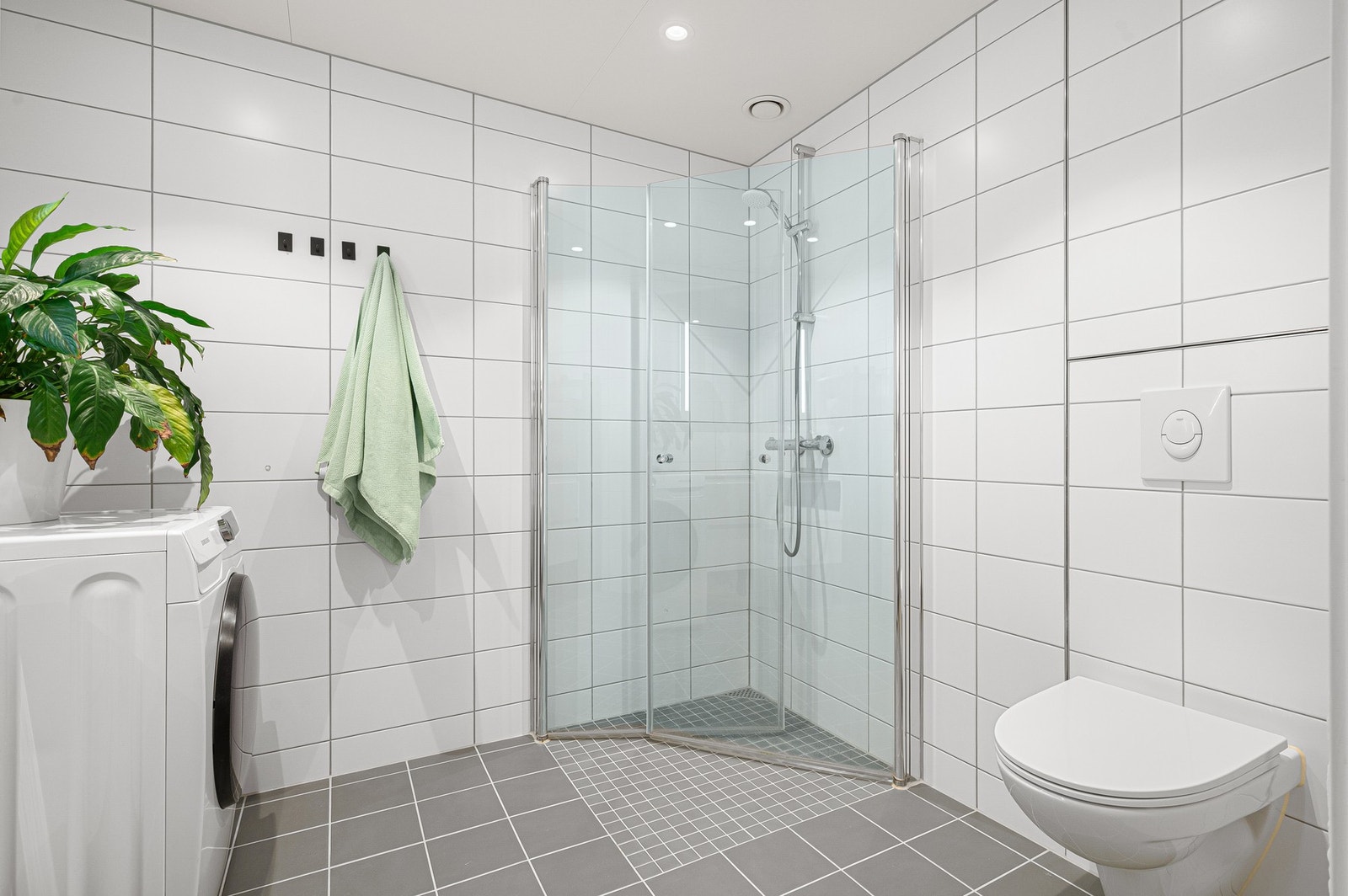 Badet er utstyr med bl.a. 2 stk dusjdører i glass, veggmontert WC, servantplate på underskap og speil. Galleribilde