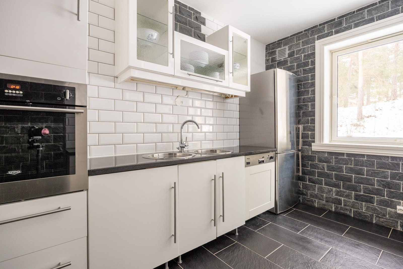 Praktisk kjøkkeninnredning med glatte fronter og benkeplate i stein med nedfelt kum i rustfritt stål. Galleribilde