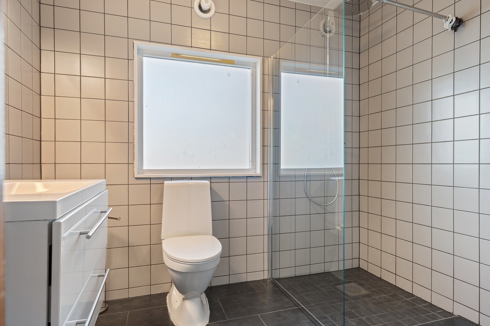 Bad 1. Etg.: Flislagt bad med baderomsinnredning med dobbel underskuff, wc, elektrisk vifte samt dusjnisje med regnvannsdusj og glassvegg. Galleribilde