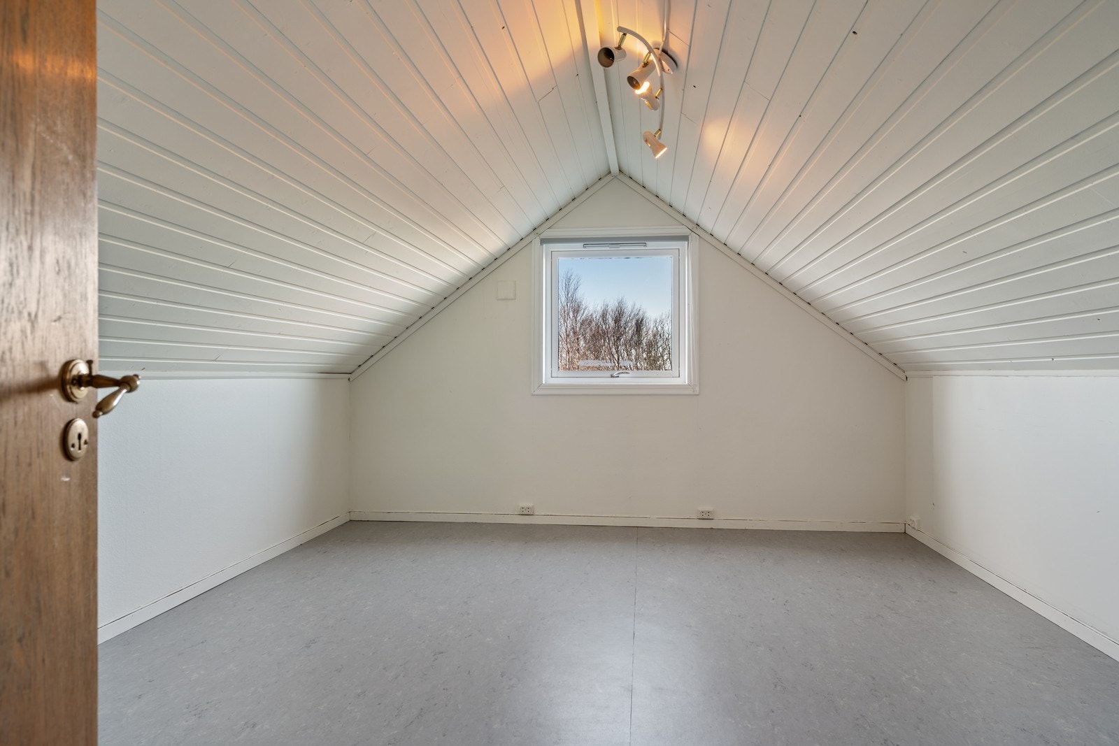 Stort soverom med plass til både dobbeltseng, skrivepult og sofagruppe. Belegg på gulv, malt panel på skråtak og tapetserte vegger. Galleribilde