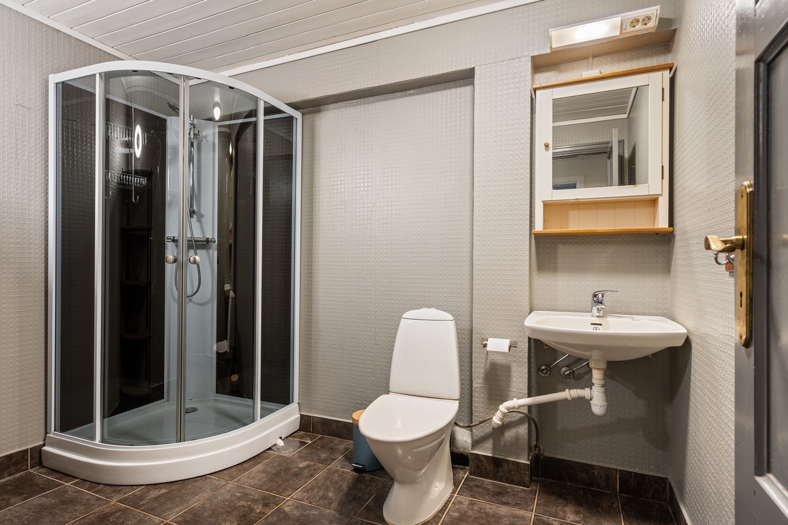 Bad U. Etg.: Bad med fliselagt gulv, dusjkabinett, wc, liten servant og speilskap. Tapetserte vegger og malt panel i tak. Galleribilde